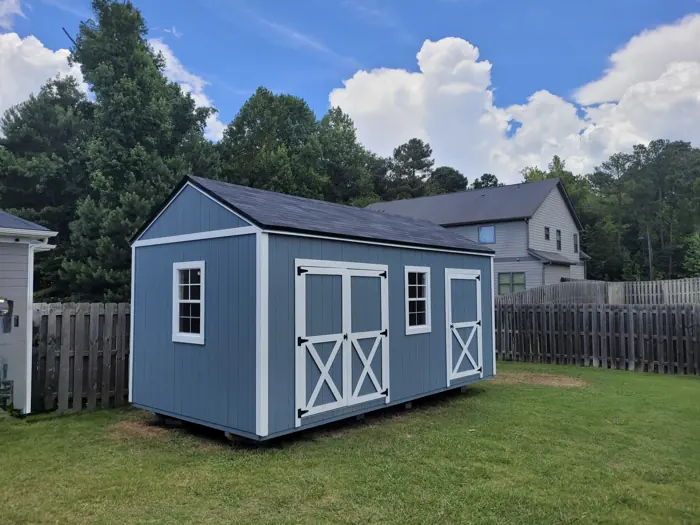 Blue wood shed with white trim, double doors with X bracing and a second single door, in a fenced backyard